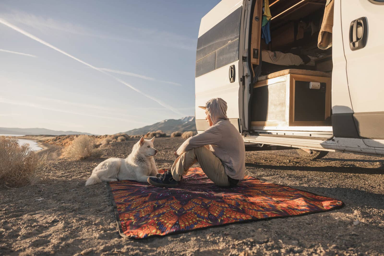 RV Life guy with dog sitting on Tarpestry outside camper in the desert.